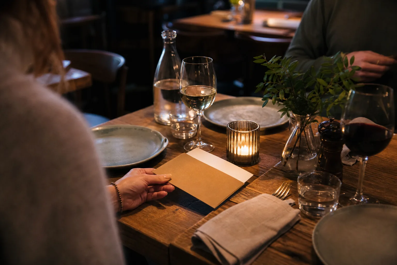 Ett kuvert med ett värdebevis läggs bredvid ett dukat restaurangbord med ett litet levande ljus