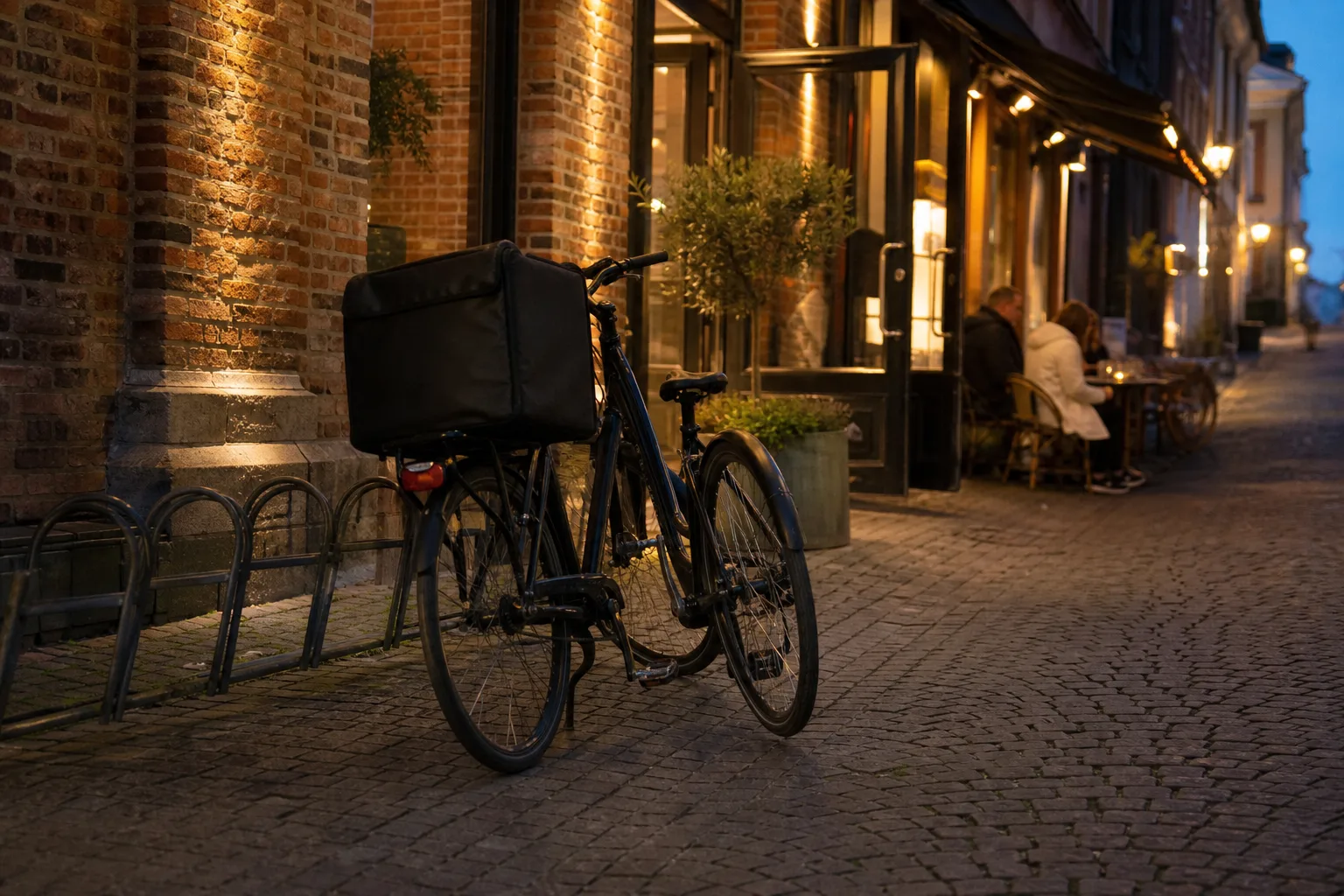 Leveranscykel parkerad utanför en tänd restaurangentré i centrala Malmö på kvällen