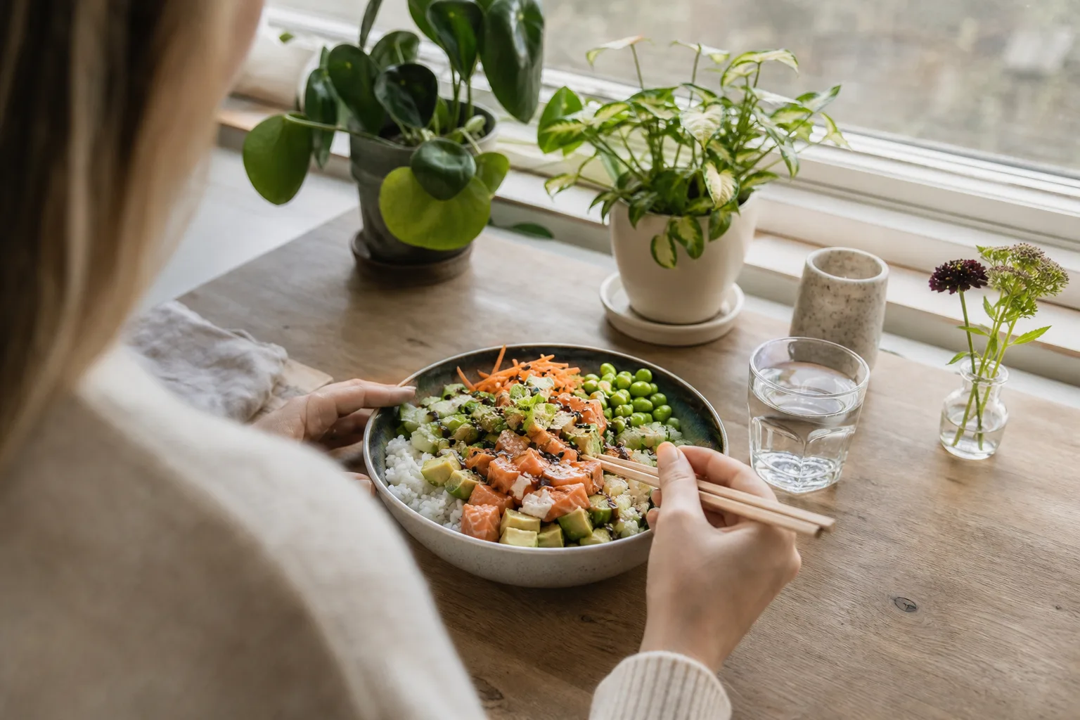 En pokébowl med ris, lax, avokado och edamame uppdukad på ett köksbord hemma, dagsljus genom fönstret