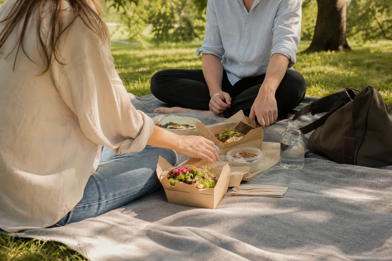 En picknickfilt i en park med uppackade takeaway-lådor och en axelväska bredvid